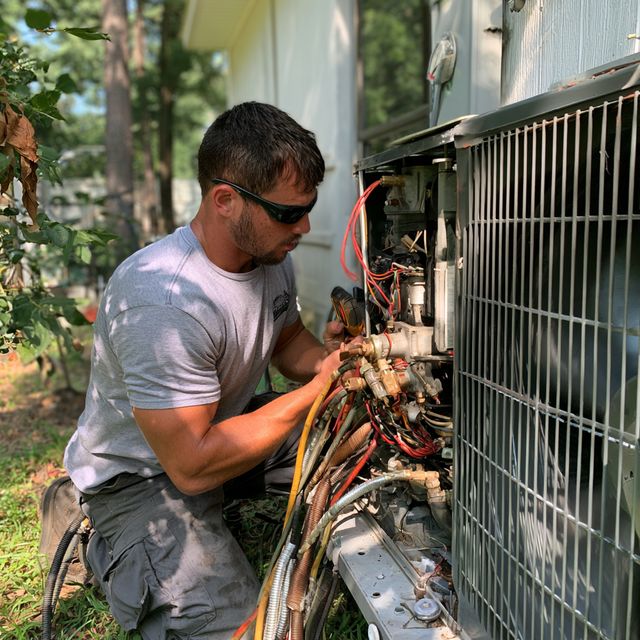 HVAC technician in safety glasses checking wiring inside an outdoor condenser unit