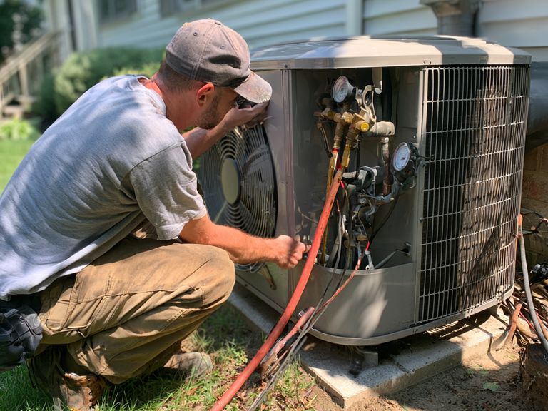 HVAC technician reading pressure gauges connected to an outdoor air conditioning unit