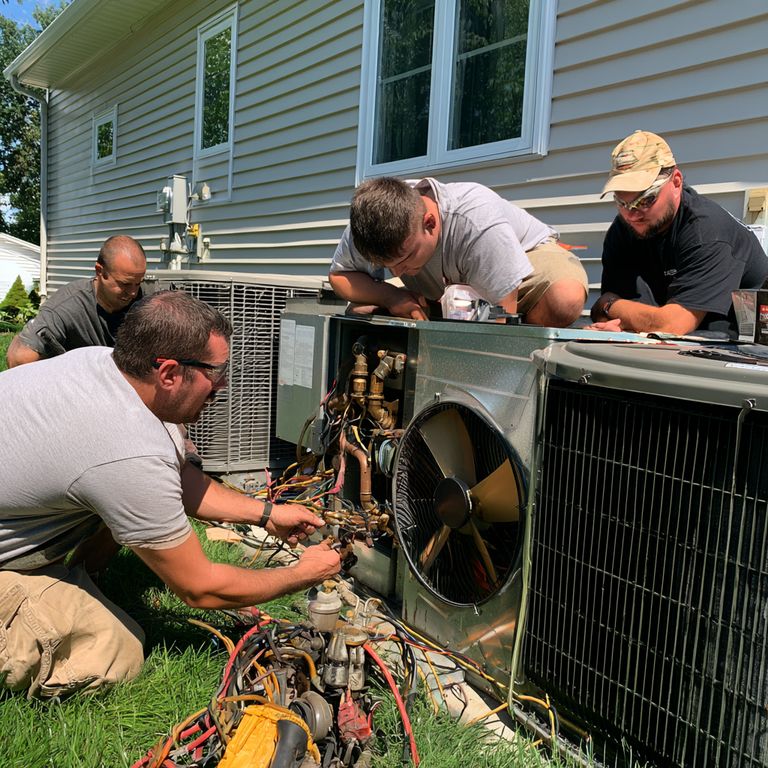 Four HVAC technicians working together on outdoor air conditioning units beside a house